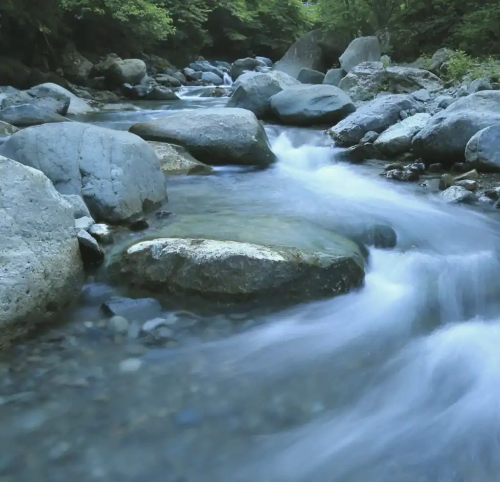 Ein klarer Gebirgsbach, der über Steine fließt – Symbol für den energetischen Fluss und die umfassende Feng Shui Transformation.